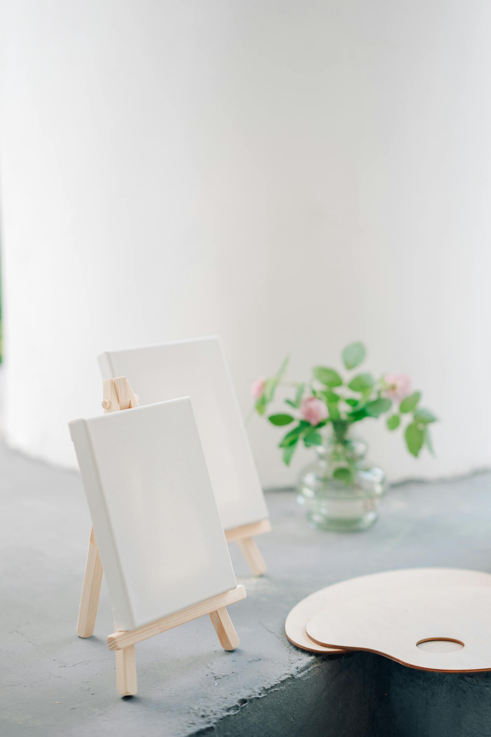 A minimalist art setup featuring small canvas easels and a vase with pink flowers.